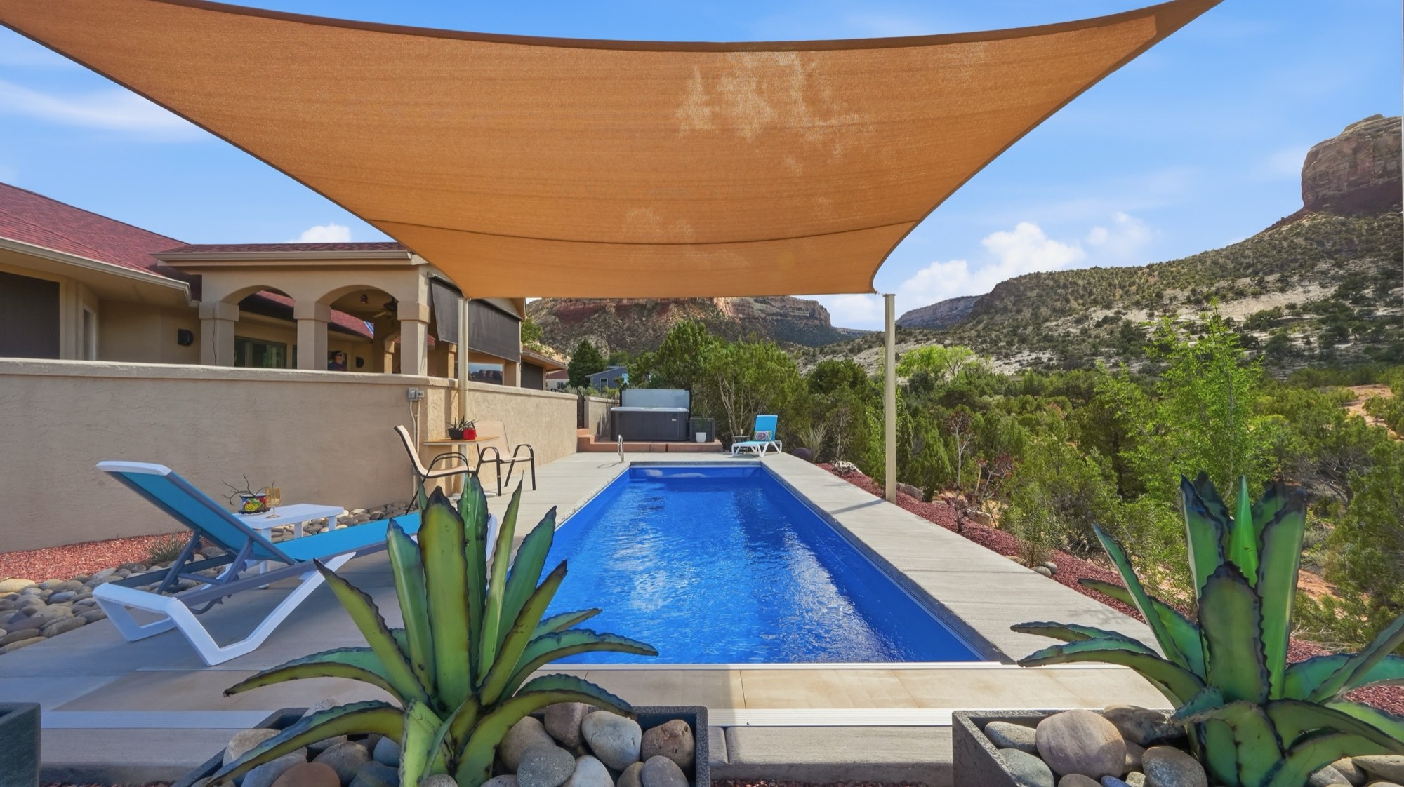 A tan shade sail over a backyard lap pool, with red-rock cliffs behind